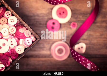 A close up of a box of pink and white buttons, with a pink polka dot ribbon alongside. Filtered to have a faded nostalgic look. Stock Photo