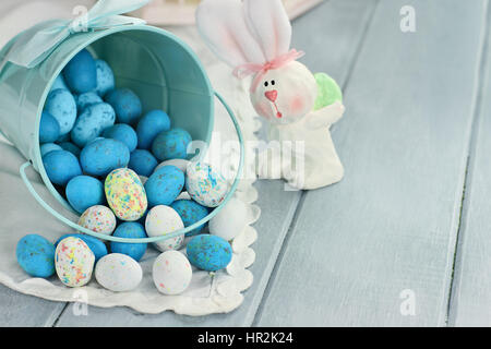 A blue tin bucket tipped over, spilling Easter candy eggs onto a table. Shallow depth of field. Stock Photo