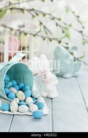 A blue tin bucket tipped over, spilling Easter candy eggs onto a table. Shallow depth of field. Stock Photo