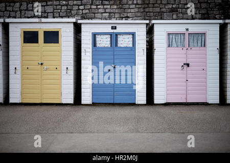 Three white beach huts with coloured doors on the sea front. Stock Photo