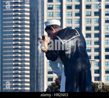 Bronze, 25-foot 'Unconditional Surrender' statue of an American sailor kissing a nurse near USS Midway Museum with partial skyline of San Diego. Stock Photo
