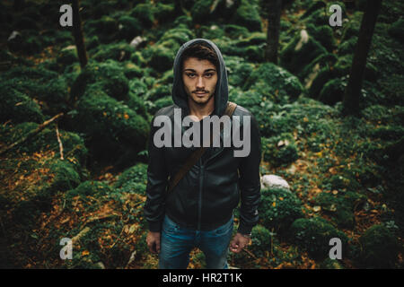 Young hooded cool man in the woods, rocks and trees on background Stock Photo