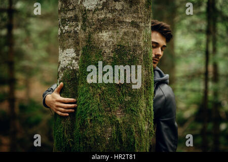 Young man relaxing in the forest and hugging a moss covered tree Stock Photo