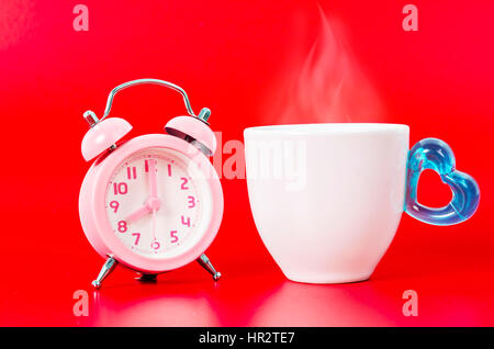 Vintage pink alarm clock with hot coffe and smoke on red background. Stock Photo