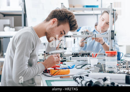 Engineering students working in the lab, a student is using a voltage and current tester, another student in the background is using a 3D printer Stock Photo