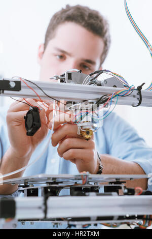 Young engineer in the laboratory working on a 3D printer and checking wires, education and innovation concept Stock Photo