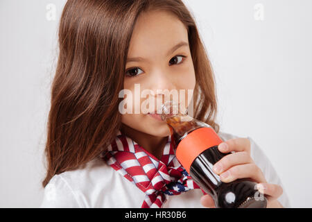 Enjoying drink. Happy little lively girl expressing happiness and drinking the soda pop while standing against white background Stock Photo