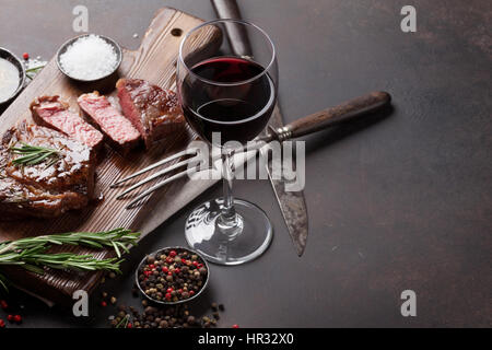 Grilled ribeye beef steak with red wine, herbs and spices on stone table Stock Photo