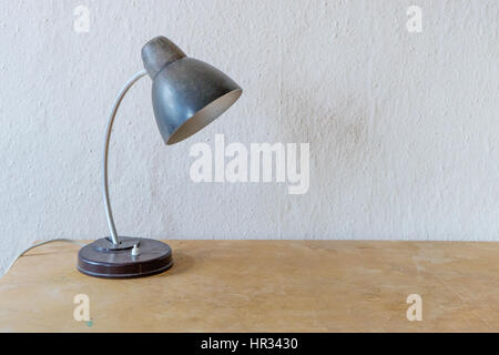 Old table lamp on a wooden table in front of a white wall Stock Photo