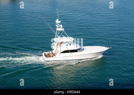 White cabin cruiser speeding across blue water in harbor Stock Photo