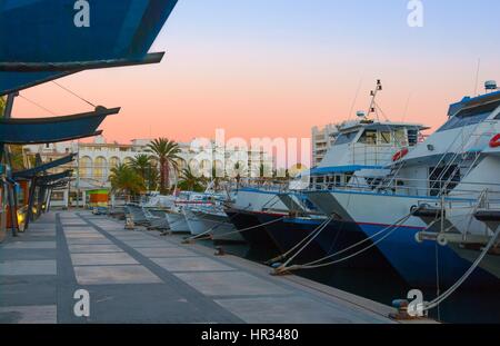 Boats in for the evening in marina harbor under dramatic magenta sunset color .  End of a warm sunny day in Ibiza, St Antoni de Portmany, Spain. Stock Photo
