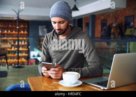 Young handsome hipster guy at the restaurant using a mobile phone. Stock Photo