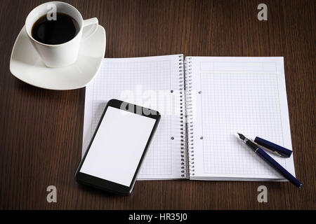 Top view on opened notebook, smartphone, pen and cup of coffee on dark wooden office desk. Stock Photo