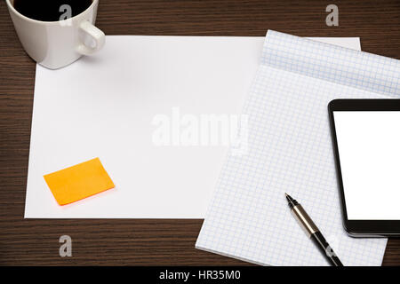 Modern smartphone with blank screen, notepad, sheet of paper, sticky note and cup of coffee on dark wooden office desk. Stock Photo