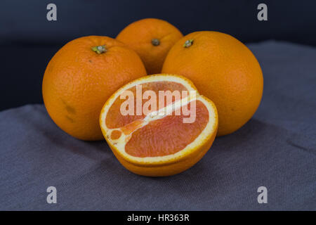 Cut Orange with three whole oranges on gray fabric Stock Photo