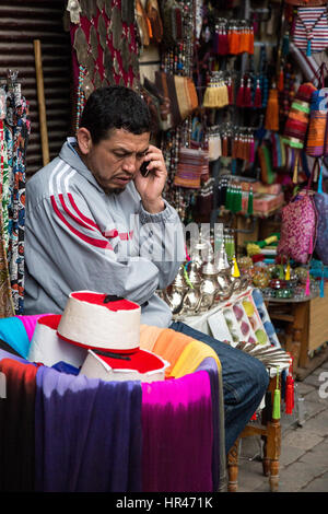 Marrakesh, Morocco.  Shop Vendor of Fezzes, Tea Pots, and Decorative Items Listening to his Cell Phone. Stock Photo