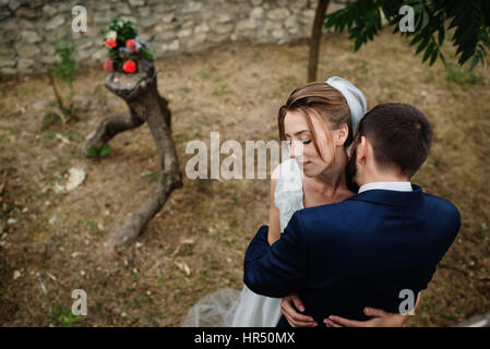 Groom kissing bride on neck background wooden stump with wedding bouquet. Stock Photo