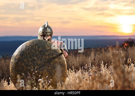 Ancient Greek soldier holding a sword hiding behind his shield on the battlefield ready to attack copyspace. Spartan warrior on the battlefield beauti Stock Photo