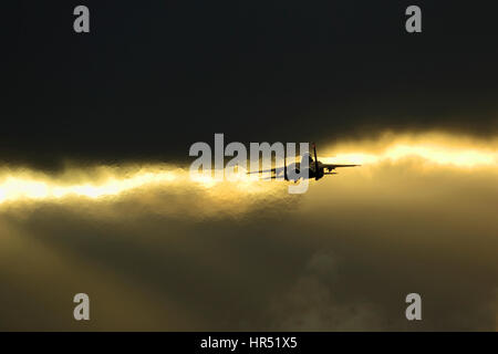 McDonnell  Douglas Boeing F15E Strike Eagle flying through gaps in clouds backlit by the setting sun Stock Photo