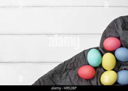 Overhead view of colorful Easter eggs over a wood table top with grey fabric. Flat lay style. Stock Photo