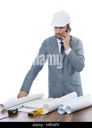 Important calls. Professional male engineer talking on his mobile phone while working on building blueprints isolated on white profession development  Stock Photo
