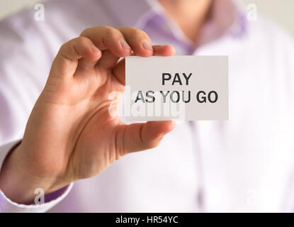 Closeup on businessman holding a card with PAY AS YOU GO message, business concept image with soft focus background and vintage tone Stock Photo