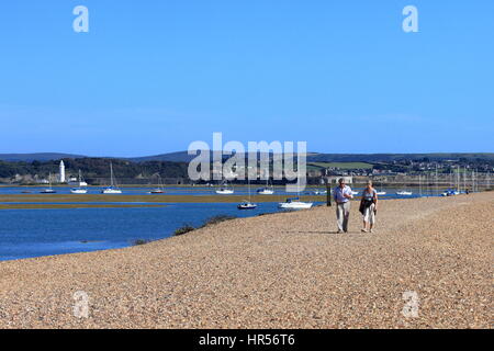 Couple on return stroll along shingle bank from Hurst Castle and lighthouse to Keyhaven with Isle of Wight distant backdrop Stock Photo