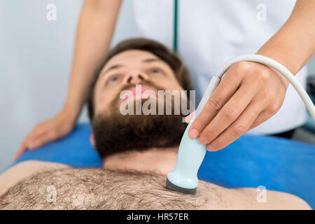 Midsection of female doctor placing ultrasound probe on male patient's chest in clinic Stock Photo