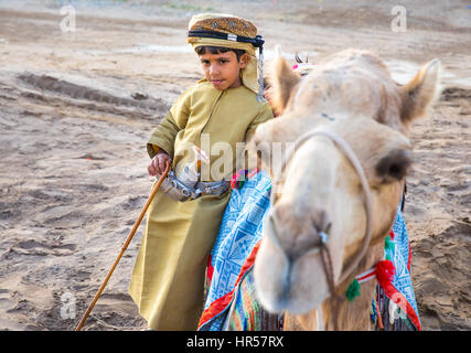 Muscat, Oman - Feb 4, 2017: Young Omani boy dressed in traditional clothing posing next to his camel. Stock Photo