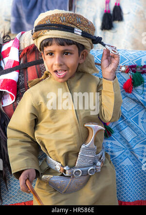 Muscat, Oman - Feb 4, 2017: Young Omani boy dressed in traditional clothing posing next to his camel. Stock Photo