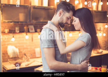Young beautiful couple in kitchen. Family of two hugging while preparing food. Man and woman standing forehead to forehead. Nice loft interior with li Stock Photo
