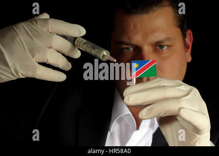 Young businessman gives a financial injection to Namibian flag isolated on black background Stock Photo