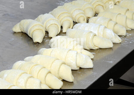 A baker working on a floured surface, rolling up dough squares into croissant shapes before baking Stock Photo