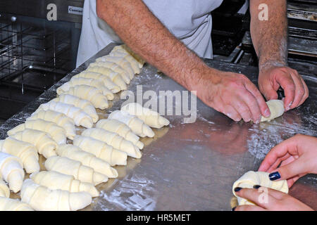 A baker working on a floured surface, rolling up dough squares into croissant shapes before baking Stock Photo