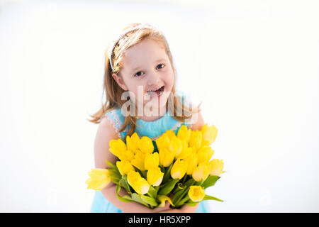 Cute little girl in blue dress holding tulip flowers bouquet on birthday party. Spring and Easter decoration. Child with yellow flowers. Kid with spri Stock Photo