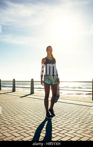 Full length shot of young woman walking on the sea side promenade. Female runner out in the morning. Stock Photo