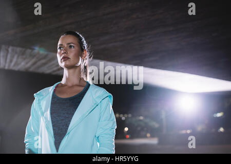 Portriat of urban female runner standing under bridge at night. Beautiful young woman standing on the street. Stock Photo