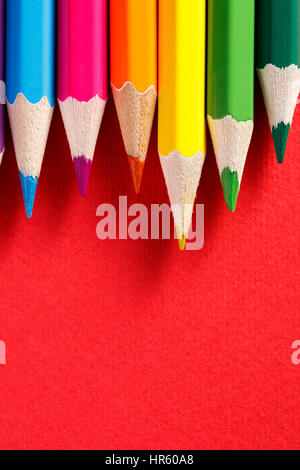 colored pencils lying in row on red background Stock Photo