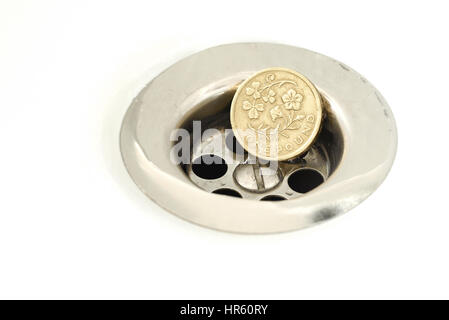 Single British Pound Coin resting in a silver plughole with water droplets on the coin and white ceramic surface Stock Photo