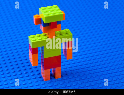 Man,  boy, male with jug-ears and a green cap built of Lego bricks on a blue Lego base plate -  dabbling or wading in blue water Stock Photo