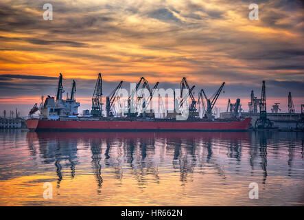 Ship and cranes in port at sunset. Cargo ship terminal at twilight scene. Stock Photo