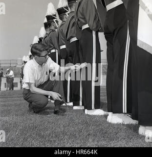 1950s, historical, college football match, a young man with scissors and brush kneels down to check the trousers of the marching bandsmen who provide the traditional entertainment before and during a match. Stock Photo