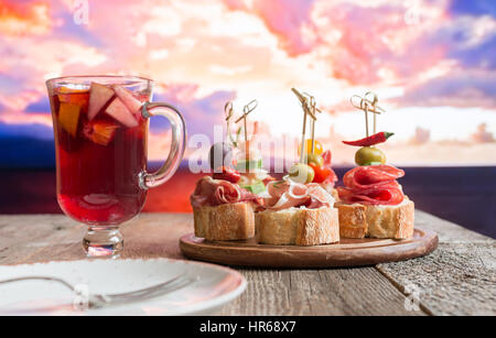 Set of Spanish tapas served on a sliced baguette with sangria on wooden table against the sea Stock Photo