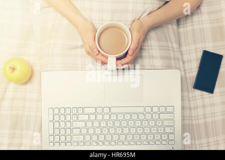 lazy sundays - woman drinking coffee and using laptop in bed Stock Photo