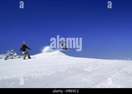 Two snowboarders jump in snow park at ski resort on sunny winter day. Caucasus Mountains, region Dombay. Stock Photo