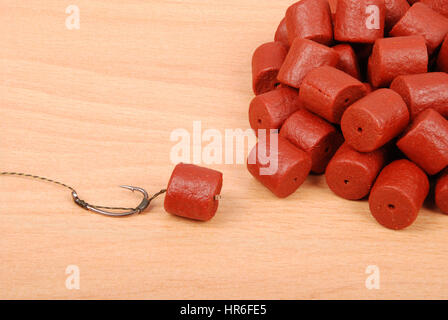 Fishing bait with hook and red pre-drilled halibut pellets for carp fishing isolated on wood background with soft shadow Stock Photo