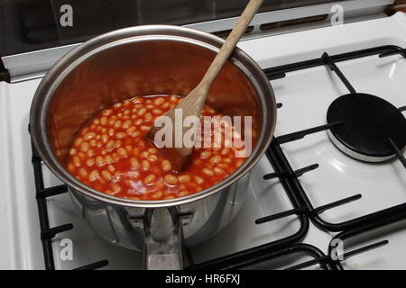 Saucepan of baked beans cooking on a gas oven hob with wooden spoon Stock Photo