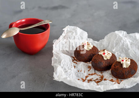 Cakes made of chocolate on a white transparent paper on a gray background. Cakes decorated with red jelly and delicate white cream. Red cup of coffee. Stock Photo