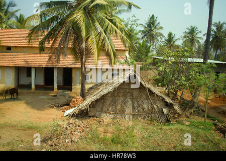 Dwelling in Indian province. New house under tiled roof in vicinity of primitive shed of palm mats Stock Photo