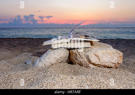 Open book at beach on a pile of books near the sea during summer sunset Stock Photo